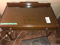 Top view of brown wooden desk showing glass top with small hole at center, raised back lip and polished finish.