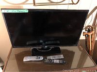 RCA flat screen television on a reflective table with three remote controls in front of it.