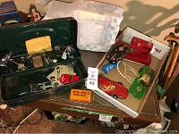 Vintage mini car lot including metal carrying case with mechanical parts, a red mini sewing machine with power cord, multiple mini cars in various colors, and a Bottoms Up Girl figure.