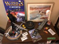 Wide view of various items on a table including Clarence Tillenius print, model airplanes, coal statue, toy cars, and a tire.