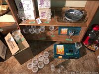 Overview of lot showing boxed crystal glass sets on shelves, loose goblets and dessert bowls on floor, and bakeware on lower shelf.