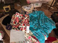 Photo showing various vintage womens clothes including floral printed tops, scarves, and a teal blue embroidered jacket.