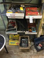 Photo of metal shelving with multiple boxes holding vintage train sets, tracks, and model trains; a yellow boxed Atlas turntable is visible on the floor below along with a black power/control unit in a box.