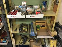 Photo of middle and lower shelves of yellow metal shelving unit containing assorted tools, boxes of nails, hardware, power tools, and hand tools.