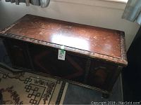 Overview of the vintage cedar chest showing the top surface and carved trim with signs of wear and scratches.