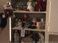 Shelf with multiple Santa figurines, two gold decorative candles, and a ceramic snowman, plus a small decorative house figurine