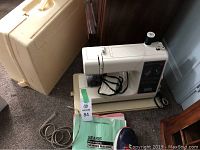 Overall view of the Kenmore sewing machine with carrying case and power cord on carpeted floor.