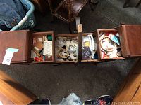 Wooden three-compartment sewing box opened up showing extensive sewing supplies inside each compartment. Handle is broken as noted.