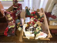 Box of assorted Christmas ornaments and vintage decor items on a table, including Santa figures, glass baubles, and small decorative pieces.