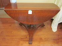 Table closed, leaf down, showing half-circle top resting on tripod pedestal base with small casters.