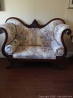 Front view of the antique Empire style settee showing floral fabric upholstery, carved wooden frame, and bolster pillows.