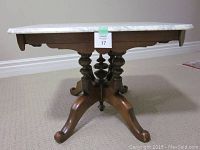 Side view of antique coffee table showing white and gray Montreal marble top and ornate turned wooden legs with curved feet.