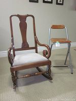 Wooden Queen Anne style rocking chair with cushioned seat and one replaced arm in darker wood, next to Ikea metal and wood bar stool.