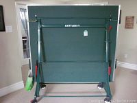 Table folded upright showing frame, wheels, and Kettler logo