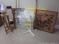 Photo of wooden plant stands, white metal shoe rack, standing fan, and framed mirror with floral tapestry