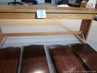 Small child's solid oak bench with light natural finish and slatted seat, placed behind bed rails.