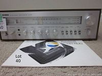 Front view of Yamaha AM/FM stereo receiver CR-600 showing tuning dial, volume and tone controls, speaker switches, and original manual in front.
