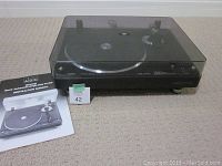 Turntable with dust cover closed, manual placed beside it.