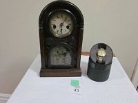 Front view of antique shelf clock and men's wristwatch displayed on black stand