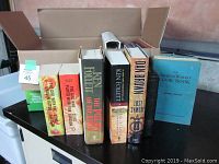 Books standing on table, showing a mix of hardcovers and paperbacks including notable authors Ken Follett and Dan Brown.