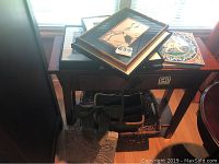 Framed photos and artwork stacked on a wooden table, with baskets visible underneath