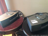 Two Bose Wave Music Systems side by side with power cords and remotes on top