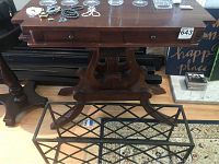 Front view of antique wood table with harp-shaped support and two drawers, showing the table top with small jewelry items and the painted metal wine rack beneath.