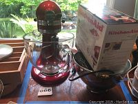 Red KitchenAid stand mixer with glass bowl and an unboxed food grinder attachment placed in a metal bowl.