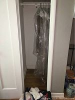 Closet view showing 6 tablecloths and 1 table runner hanging inside clear plastic garment bags.