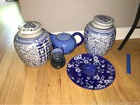 Asian inspired porcelain jars, blue teapot, small vase, floral plate and small bowl arranged on a wooden floor