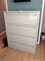 Front view of the beige HON four-drawer lateral file cabinet showing integrated handles and lock at top drawer.