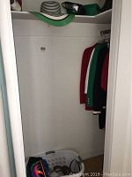 Empty closet space with a folded basket that contains shoes and accessories at the bottom right corner, some clothing items hanging on the right side of the closet space.