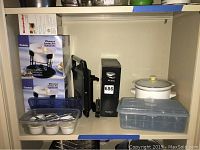 Wide shot showing Rival Crock Pot, boxed fondue sets, black waffle irons, plastic containers and candle votives on a shelf