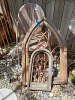 Lot showing vintage plastic lawn chair behind two rustic wooden arch yard art pieces with rusted metal inserts, on outdoor rock bed in sunlight
