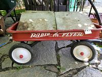 Red Radio Flyer wagon with white wheels and white lettering visible on side, showing front and side view.