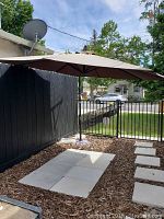 Outdoor adjustable umbrella open in daylight next to black fence and paving stones.