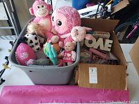 Bin with stuffed animals including pink octopus, monkey, cow, baby dolls, and small toys