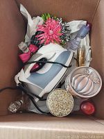 Photo showing the Black and Decker iron surrounded by fall-scented candles and various perfume bottles in a cardboard box.