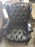 Front view of black leather tufted chair showing deep button tufted back and seat with rolled arms.