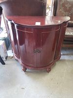 Oblique front view of reddish-brown semi-circular bar cabinet showing rounded front and double doors with metal pull handles.