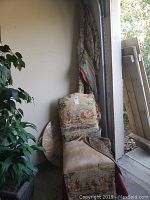 Full view of matching tapestry-style upholstered chair with some soiling on seat, curtains visible behind it, and part of glass tabletop wrapped behind chair.