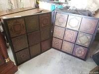 Shows two large framed wall art pieces, each containing 9 square wood panels with ornate patterns in various earth tones including browns, reds, greens, golds and blacks.