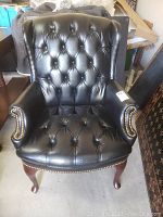 Front view of black leather tufted chair showing deep button tufting and armrests with nailhead accents.