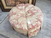 View showing top of round cushioned ottoman with red and cream toile fabric upholstery.