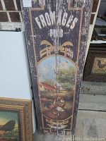 Wooden rustic farm scene sign with roosters and the words 'FROMAGES NUS' showing weathered paint.