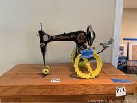 Front side view showing black and gold vintage sewing machine with bright yellow wheels attached, mounted on wooden base.