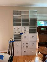 Full view of stacked cubby shelves and additional shelving units arranged together against a wall, showing various compartments and drawers, some signs of surface scratching.