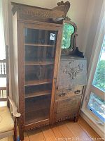 Full front view of oak secretary desk showing glass‐door cabinet on left and carved drop-front desk on right