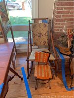 Vintage wooden rocking chair with floral fabric upholstery on seat and back, showing wear and scratches, placed indoors near window and fireplace.