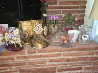 Photo showing lot contents on brick hearth including clocks, art glass carousel horse, glass dishes and flower arrangements.